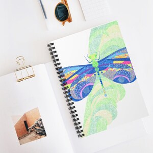 May include: A colorful dragonfly with blue, green, pink, and yellow wings is drawn on a white background. The dragonfly is surrounded by a green and white swirl pattern.