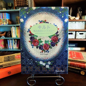 May include: A book titled "キルト 布と糸のシンフォニー QUILTS" by Sachiko Argu and Kyata Shain. The cover features a blue and white quilt with a floral design.