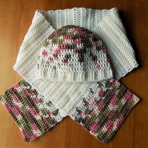 May include: A white crocheted hat and scarf set with pink, green, and brown accents. The hat is a simple beanie style and the scarf is a long, rectangular shape.