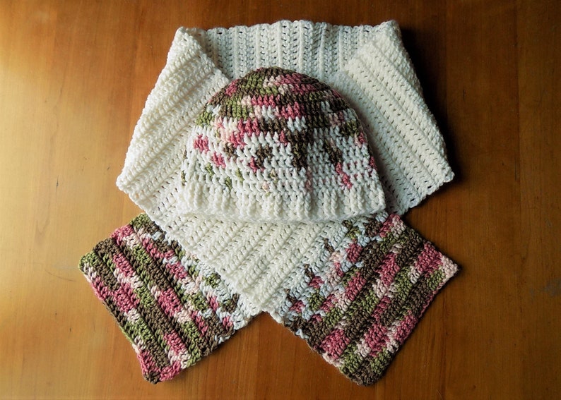 May include: A white crocheted hat and scarf set with pink, green, and brown accents. The hat is a simple beanie style and the scarf is a long, rectangular shape.