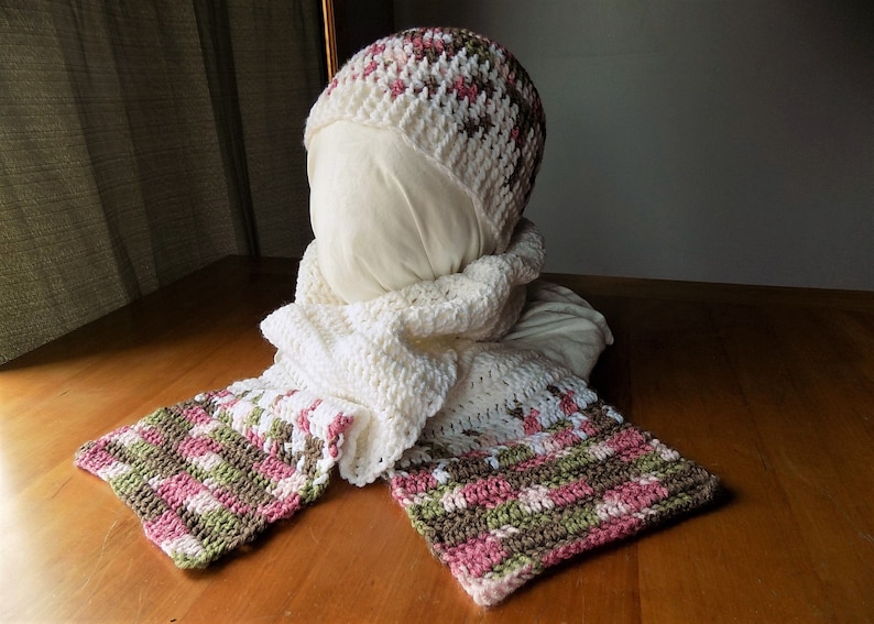 May include: A white crocheted hat with pink and brown stripes, and a matching scarf with pink, brown, and white stripes.