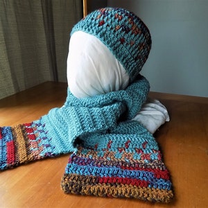May include: A teal blue crocheted hat and matching scarf with brown, red, and purple accents. The hat and scarf are made with a textured stitch.