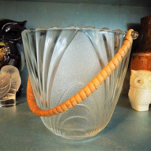 May include: A clear glass ice bucket with a woven wood handle. The bucket has a textured, fluted design.