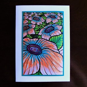 May include: A greeting card featuring a vibrant floral illustration. The artwork showcases large, stylized flowers with orange, blue, and purple petals, set against a background of green leaves. The card is framed with a teal border and a white background.