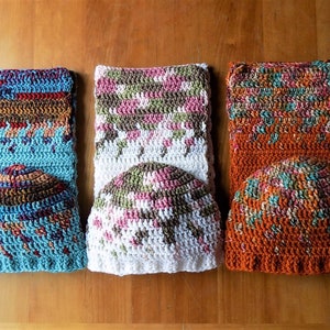 May include: Three crocheted hats in different colors and patterns. The hat on the left is blue with brown and red accents. The middle hat is white with brown, green, and pink accents. The hat on the right is orange with brown, green, and blue accents.