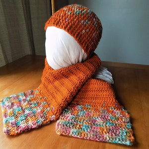 May include: A crocheted hat and scarf set in a rust orange color with a multi-colored flecked pattern. The hat is a slouchy beanie style and the scarf is long and rectangular.