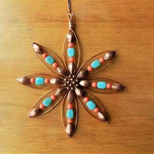 May include: A copper wire star ornament with turquoise and coral beads. The star has six points and is decorated with small copper beads in the center.