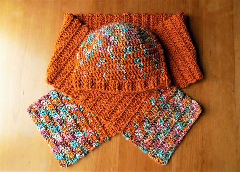 May include: A crocheted hat and scarf set in a rust orange color with a multi-colored yarn pattern. The hat is a slouchy beanie style and the scarf is a long, rectangular shape.