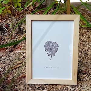 Peut inclure: Un cadre en bois clair encadre une impression d'une feuille noire et blanche sur fond blanc. Le texte « Belle à croquer » est imprimé en bas de l'image.