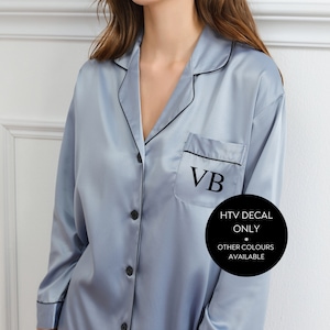 May include: A light blue satin pyjama top with black trim and a black pocket on the left side. The pocket has the initials "VB" embroidered in black. The text "HTV DECAL ONLY" and "OTHER COLOURS AVAILABLE" is printed in black on a white circle.