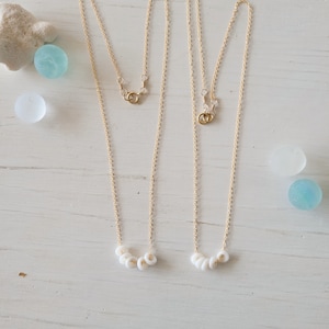 Könnte beinhalten: Zwei goldene Kettenhalsketten mit weißen Perlenakzenten. Jede Halskette hat fünf weiße Perlen in einer Reihe.