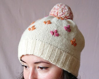 Hand knitted white wool beanie hat with floral embroidery and pom pom