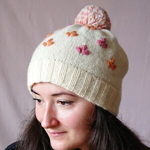 Handgestrickte weiße Beanie-Mütze aus Wolle mit Blumenstickerei und Bommel