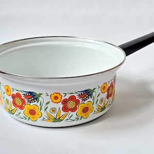 May include: White enamel saucepan with a black handle and a floral design in red, yellow, and blue.