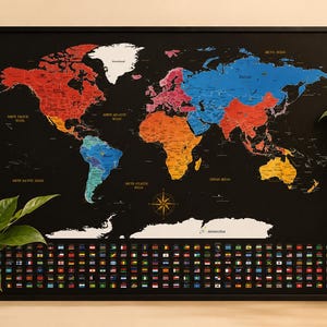 May include: A framed world map with a black background, showing continents in different colours. The map includes country flags along the bottom and ocean names. A compass rose is in the centre. The frame is black.