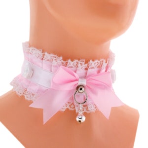 May include: A pink and white lace choker with a satin bow and a silver bell charm.