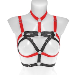 May include: A red and black harness with adjustable straps and metal hardware. The harness features a choker-style neckline and a series of intersecting straps across the chest and torso. The design is displayed on a white mannequin.