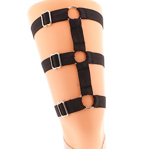May include: Black thigh garter with three adjustable straps and silver metal rings.