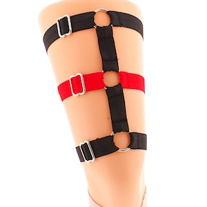 May include: Black and red adjustable garter belt with silver metal rings. The garter belt is made of elastic material and has a simple design.