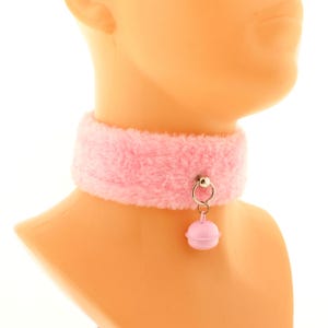 Op de afbeelding: Een roze choker van nep bont met een kleine roze belhanger en een zilveren ring.