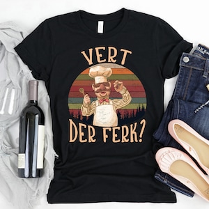 May include: Black t-shirt with a retro-style illustration of a chef with a mustache and the text "Vert Der Ferk?"