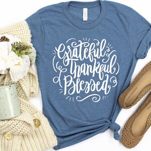 May include: A blue t-shirt with the text "Grateful & Thankful Blessed" in white lettering.