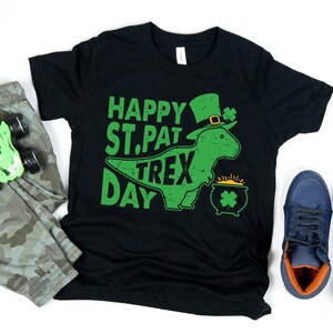 May include: Black t-shirt with a green dinosaur wearing a green hat and holding a pot of gold. The text "Happy St. Pat Trex Day" is printed on the shirt.