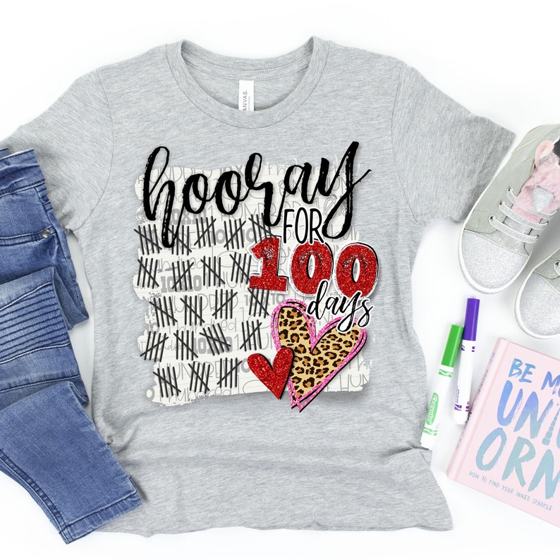 Peut inclure: T-shirt gris avec le texte "hooray for 100 days" en paillettes noires et rouges. Le nombre 100 est entour&eacute; de marques de pointage noires et roses. Il y a deux c&oelig;urs, un rouge et un imprim&eacute; l&eacute;opard, avec des accents de paillettes roses.