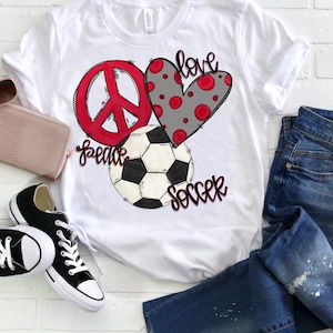 May include: White t-shirt with a red peace sign, a gray heart with red polka dots, and a black and white soccer ball. The text "peace", "love", and "soccer" are written on the shirt.