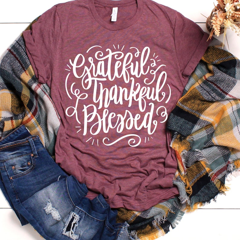 May include: A maroon t-shirt with the text "Grateful Thankful Blessed" in white cursive lettering.