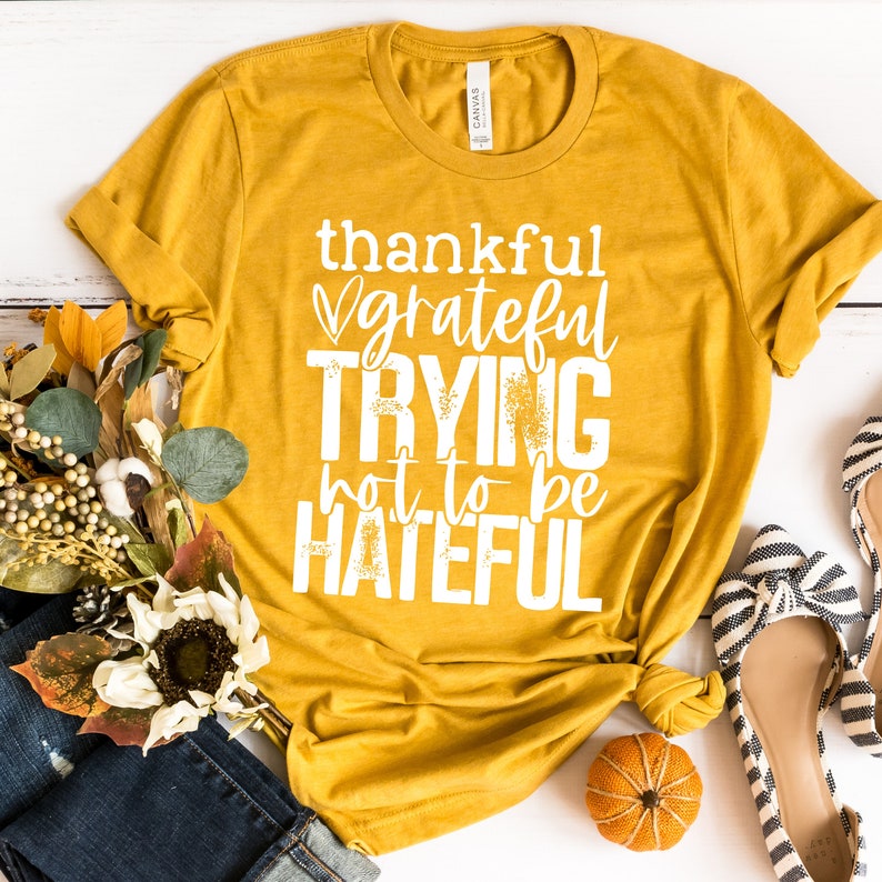 Puede incluir: Una camiseta amarilla mostaza con un gr&aacute;fico blanco que dice "thankful grateful trying not to be hateful".