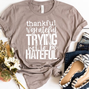 Puede incluir: Una camiseta marr&oacute;n con el texto "thankful grateful trying not to be hateful" impreso en blanco.