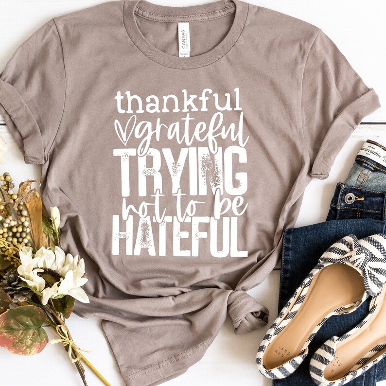 Puede incluir: Una camiseta marr&oacute;n con el texto "thankful grateful trying not to be hateful" impreso en blanco.
