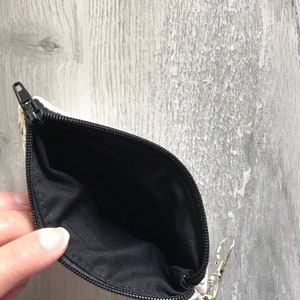 May include: A small, white zippered pouch with a black lining. The pouch is open and the lining is visible.