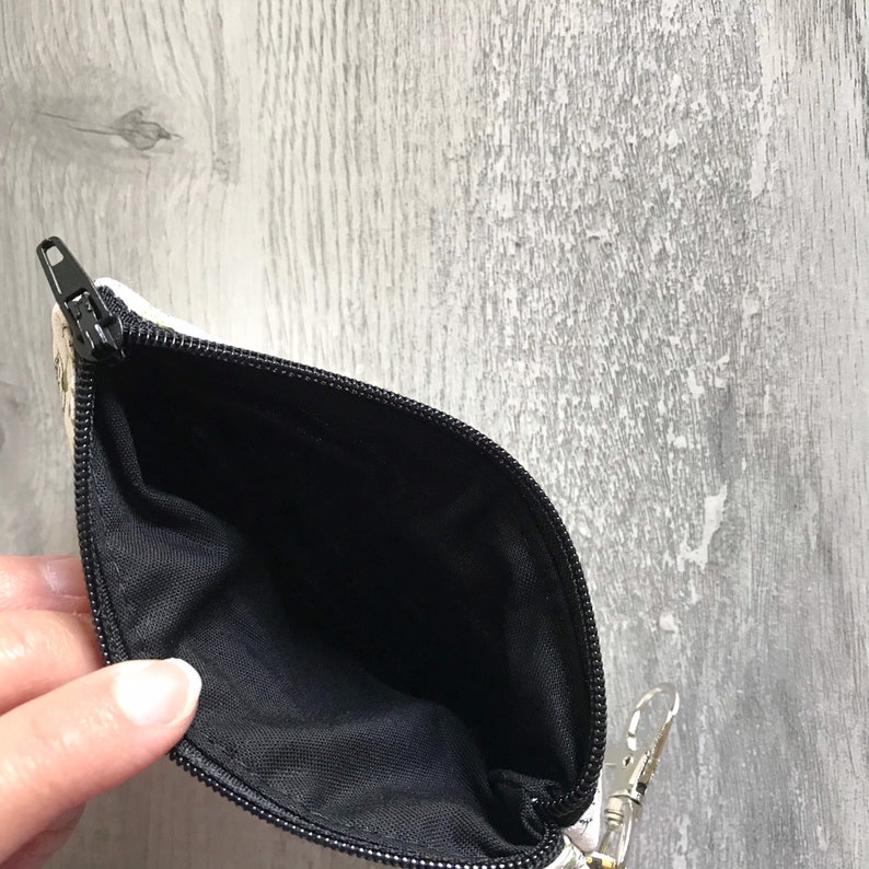 May include: A small, white zippered pouch with a black lining. The pouch is open and the lining is visible.