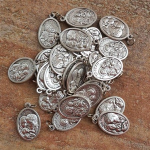 May include: A pile of silver-toned metal charms featuring an image of Saint Joseph, Mary, and baby Jesus. The charms are oval-shaped and have a loop at the top for attaching to a necklace or bracelet. The charms are all identical and feature the words "Holy Family" and "St. Joseph" on them.
