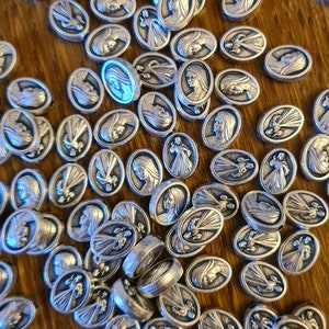 May include: A collection of silver oval-shaped charms featuring a religious image of the Virgin Mary. The charms are scattered on a wooden surface.