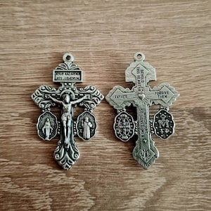 Puede incluir: Un colgante de cruz de metal plateado con tres medallones a cada lado. El lado frontal presenta un crucifijo con la inscripción "JESUS NAZARENUS REX JUDAEORUM". El lado posterior presenta la inscripción "BEHOLD THIS HEART WHICH HAS SO LOVED MEN" con un corazón y una corona de espinas. Los medallones presentan imágenes de la Virgen María, San Miguel y San José.