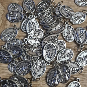 May include: A collection of silver oval-shaped charms with the words "Guardian Angel" and "St. Michael" engraved on them. The charms have a detailed design of angels with wings.