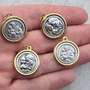 May include: Four gold-toned pendants featuring silver-toned images of Saint Joseph holding baby Jesus. The pendants are round and have a smooth, shiny finish.