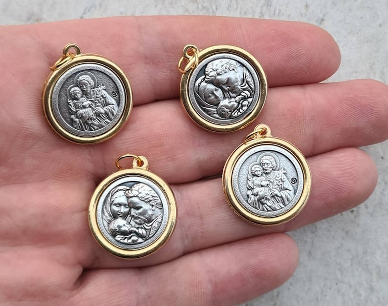 May include: Four gold-toned pendants featuring silver-toned images of Saint Joseph holding baby Jesus. The pendants are round and have a smooth, shiny finish.