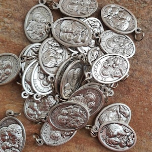 May include: A pile of silver oval-shaped charms with the image of the Holy Family. The charms have the words "Holy Family" and "St. Joseph" inscribed on them.