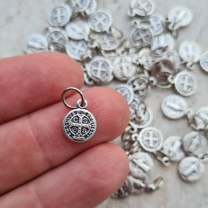 Peut inclure: Un petit charme en argent avec un motif de croix détaillé. Le charme est rond et a une boucle en haut pour l'attacher à un collier ou un bracelet.