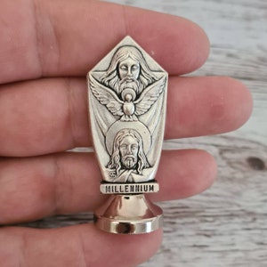 May include: Silver-toned metal religious pendant featuring a depiction of the Holy Trinity: God the Father, God the Son, and the Holy Spirit. The pendant is inscribed with the word "MILLENNIUM".