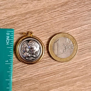 May include: A gold-toned pendant featuring a silver-toned image of a family. The image depicts a woman, a man, and a baby. The pendant is suspended from a chain.