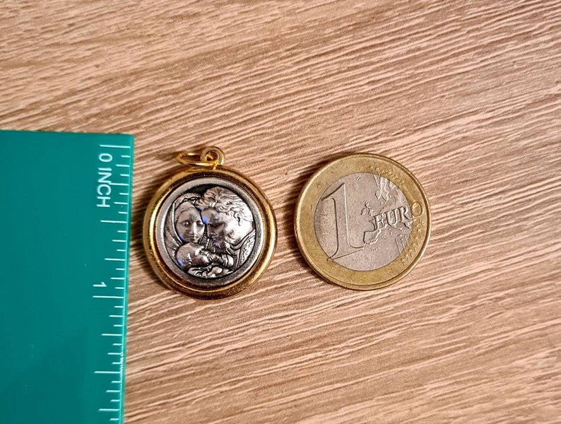 May include: A gold-toned pendant featuring a silver-toned image of a family. The image depicts a woman, a man, and a baby. The pendant is suspended from a chain.