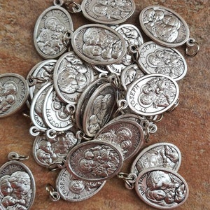 May include: A pile of silver oval-shaped charms with the image of the Holy Family. The charms have the words "Holy Family" and "St. Joseph" inscribed on them.