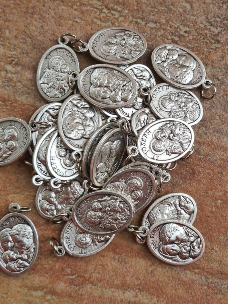 May include: A pile of silver oval-shaped charms with the image of the Holy Family. The charms have the words "Holy Family" and "St. Joseph" inscribed on them.