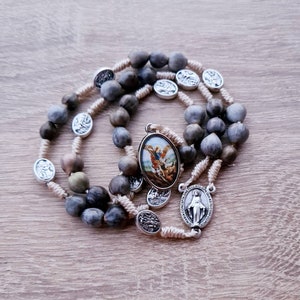 May include: A brown and gray rosary with a silver pendant featuring a religious image. The rosary is made of natural materials and has a simple design.