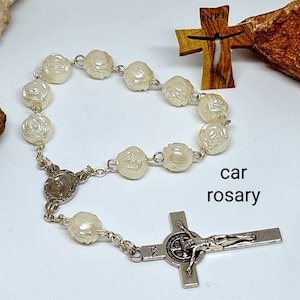 Peut inclure: Chapelet blanc avec des perles en forme de rose, un crucifix en argent avec une médaille de Saint Benoît et les mots "car rosary" imprimés en dessous.